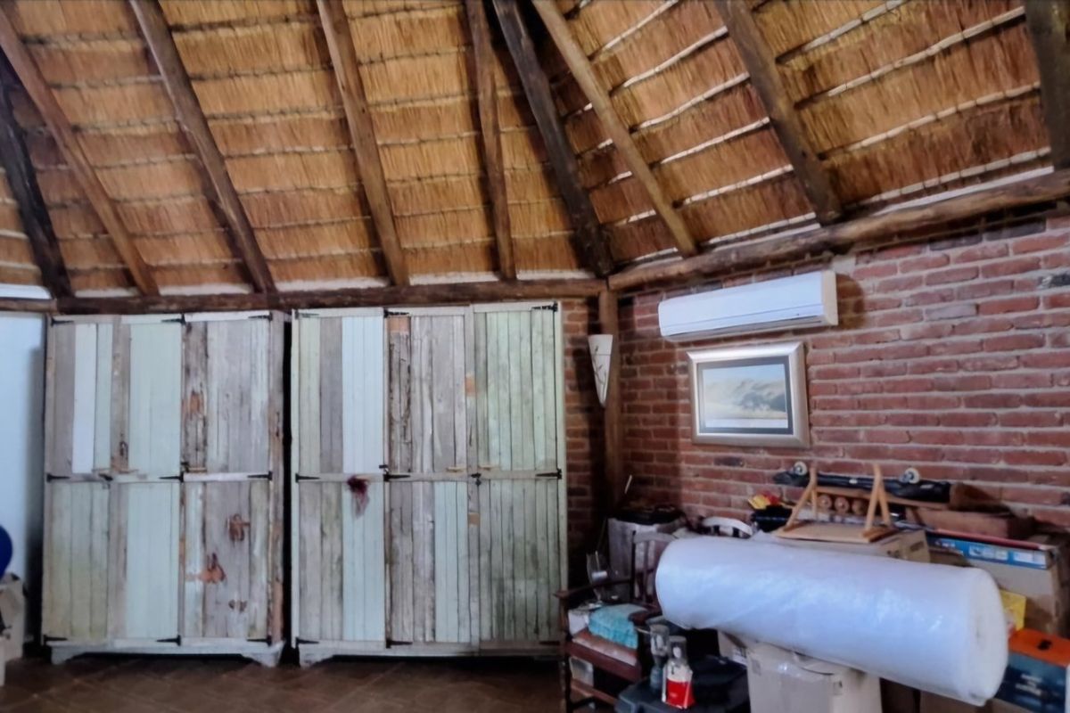 Rustic bedroom featuring a high thatched ceiling with exposed timber rafters, exposed brick walls, and built-in wooden storage cupboards.