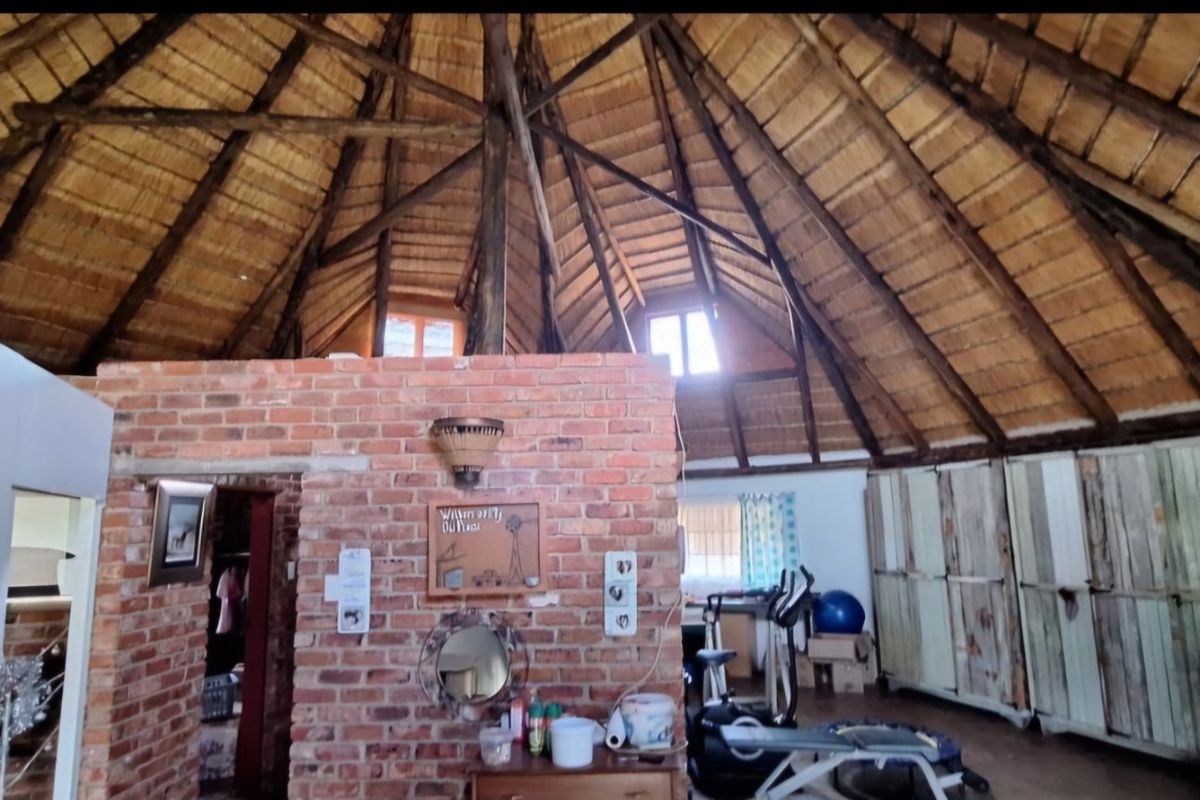 Spacious living area featuring a high vaulted thatch ceiling with exposed timber rafters and a rustic exposed brick feature wall.