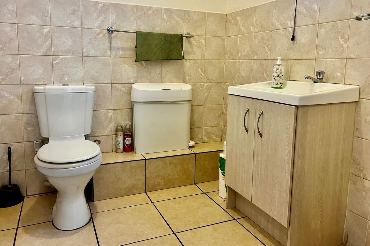 A functional bathroom featuring ceramic wall and floor tiling, a vanity cabinet with integrated washbasin, and a standard toilet.