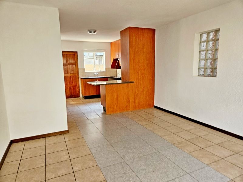 Open plan living and kitchen area featuring tiled flooring, wood-look cabinetry, granite countertops, and a unique glass block window feature.