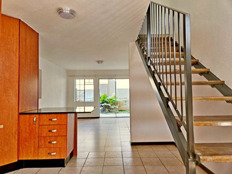 Open plan living area featuring tiled floors, a built-in kitchen cabinet unit, and a staircase with metal railings leading to the upper level.