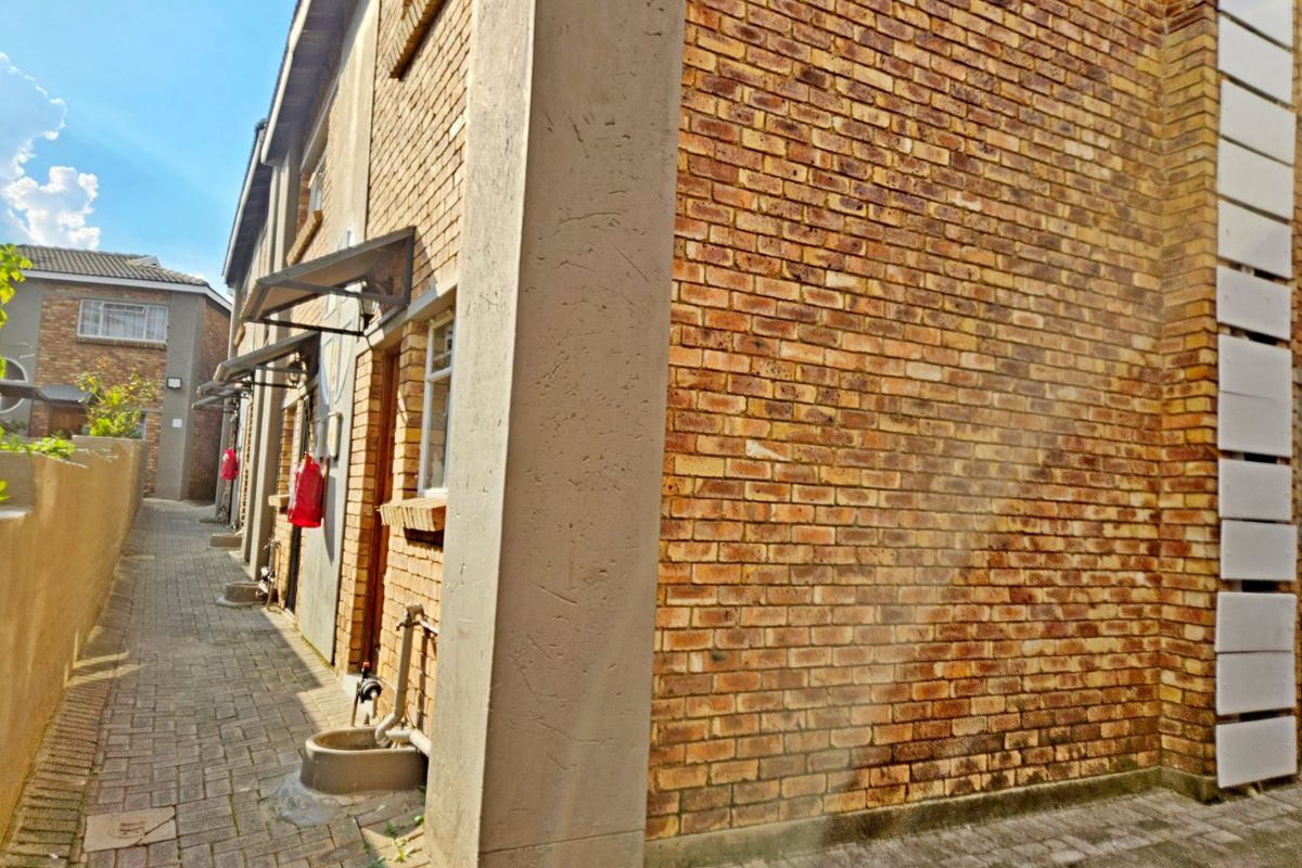 A side view of the townhouse exterior featuring face brick walls, paved pathways, and metal door awnings along the walkway.