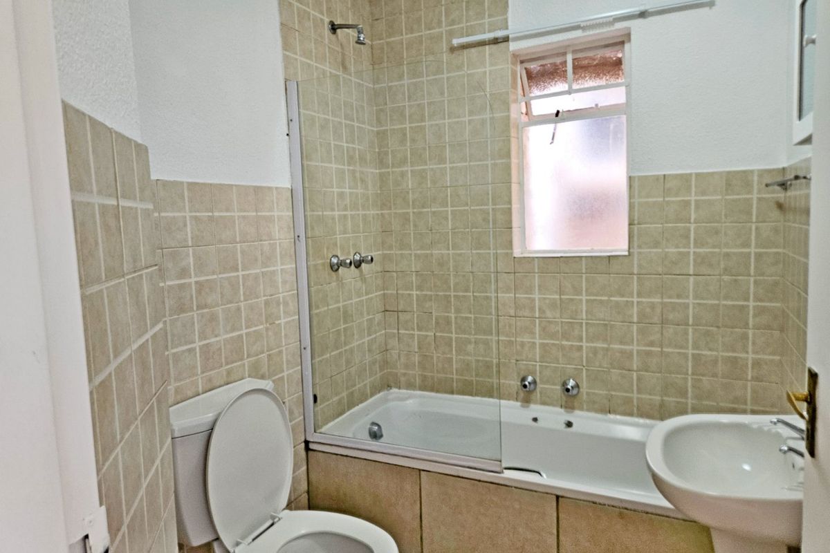 A functional bathroom featuring a combined bathtub and shower, pedestal basin, and toilet with neutral tiled finishes.