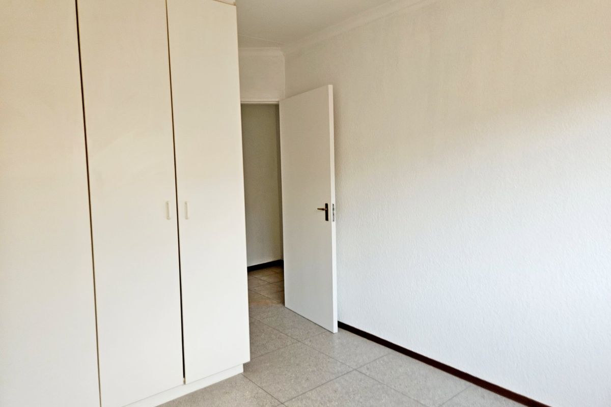 A clean, empty bedroom featuring neutral tiled flooring, built-in cupboards, and white walls, offering a blank canvas for personalization.