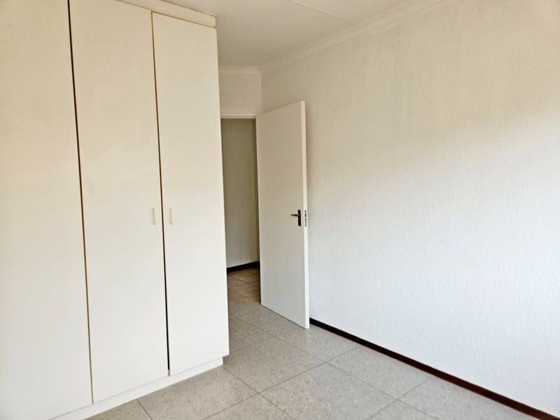 A clean, empty bedroom featuring neutral tiled flooring, built-in cupboards, and white walls, offering a blank canvas for personalization.