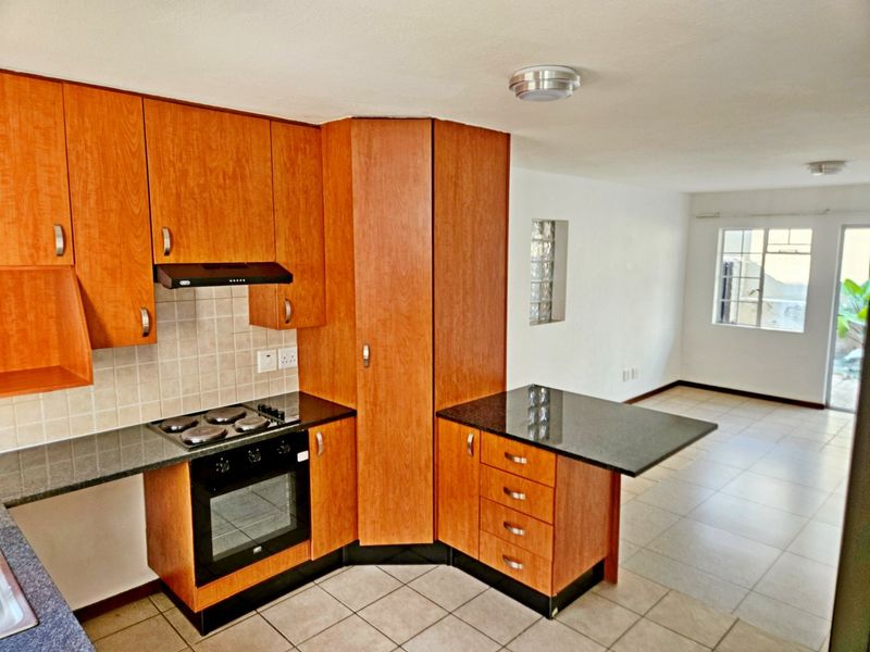 Open plan kitchen featuring wood-finish cabinetry, granite countertops, and integrated appliances, flowing into a bright, tiled living area.