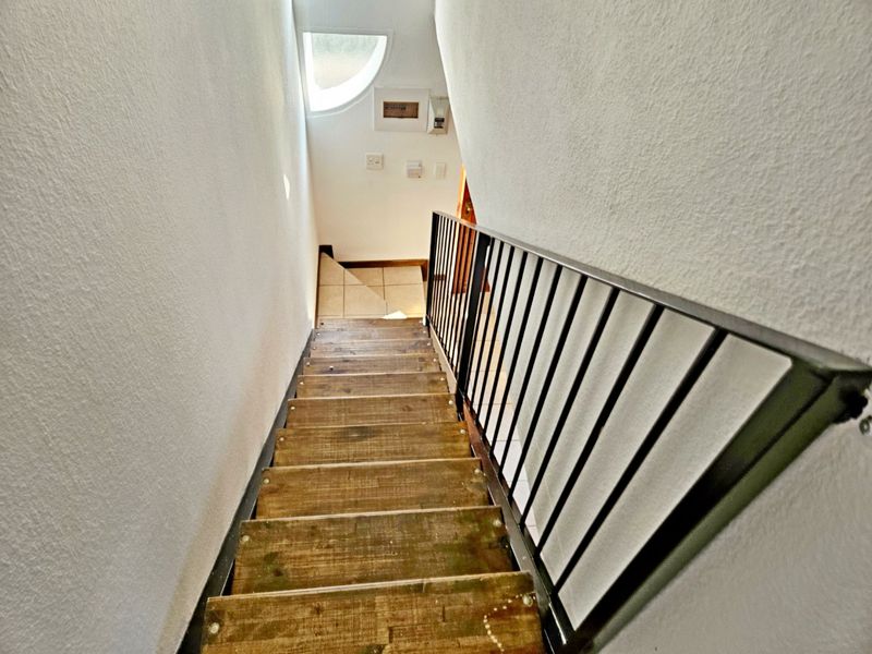 A staircase featuring wooden treads and a black metal balustrade, leading down to a landing area with a semi-circular window.