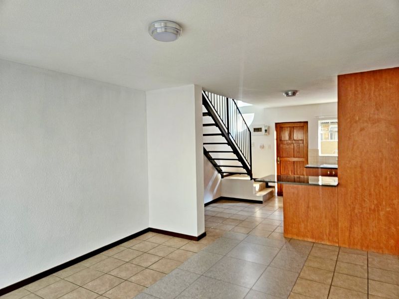 Open plan living area featuring tiled flooring, a staircase with metal balustrade, and a kitchen breakfast bar, offering a functional and versatile layout.