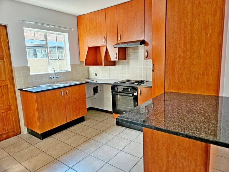 A functional kitchen featuring wooden cabinetry, granite countertops, a built-in oven with hob, and tiled flooring. The space is clean and ready for updates.