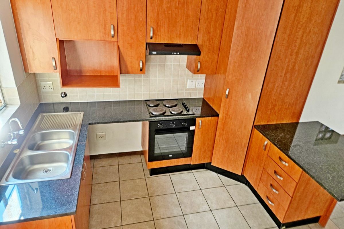 A functional kitchen featuring wood-look laminate cabinetry, granite countertops, a double stainless steel sink, and built-in electric cooking appliances.