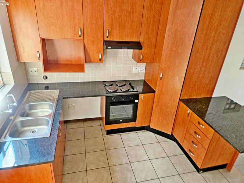 A functional kitchen featuring wood-look laminate cabinetry, granite countertops, a double stainless steel sink, and built-in electric cooking appliances.