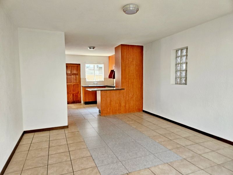 Open plan living and kitchen area featuring tiled flooring, wooden cabinetry, and a unique glass block window detail.