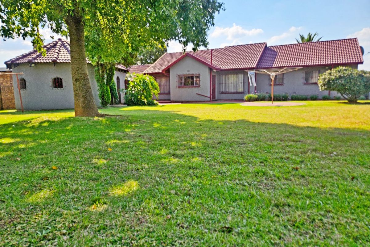 A view of the rear elevation of the house featuring a tiled roof, security bars on windows, and a spacious lawn area.