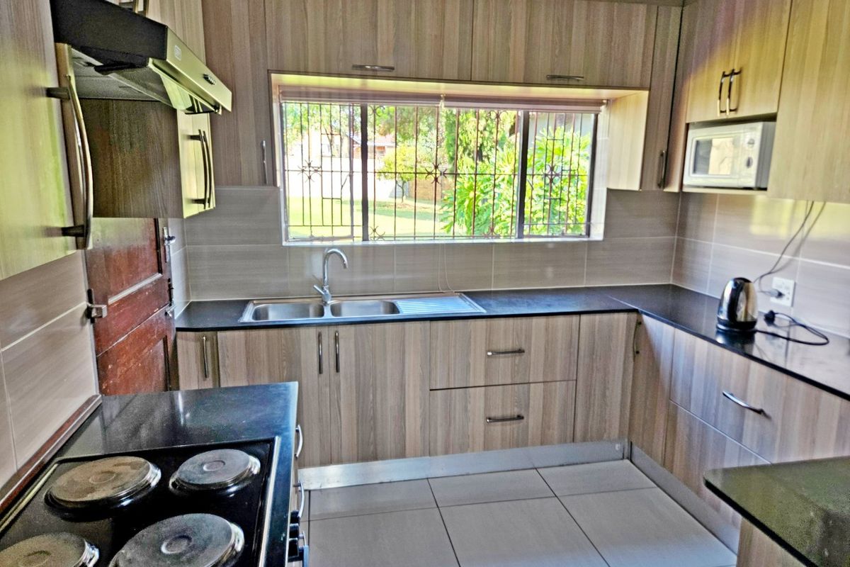 A functional kitchen featuring wood-look laminate cabinetry, granite countertops, a stainless steel sink, and built-in appliances including an electric hob and microwave.
