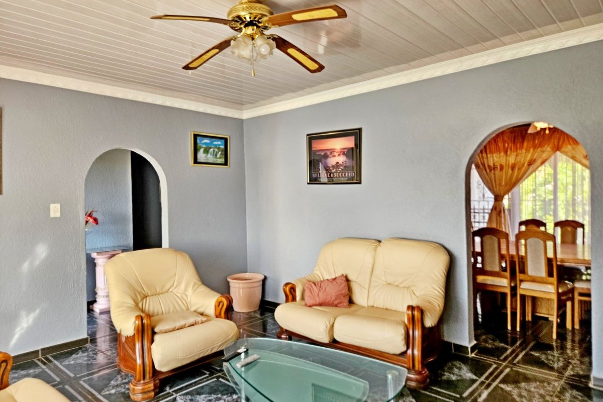 A living room featuring arched doorways, tiled flooring, and a ceiling fan, providing access to adjacent dining and hallway areas.