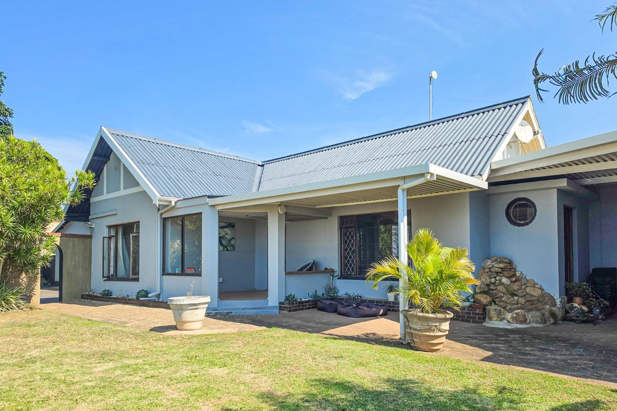 Rear view of the house featuring a covered patio area, brick paving, and a stone feature wall under a corrugated metal roof.