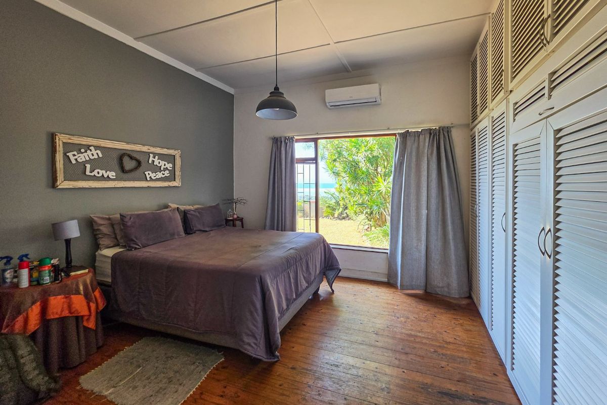 Spacious bedroom featuring hardwood flooring, extensive built-in cupboards, split-system air conditioning, and large windows offering garden and sea views.