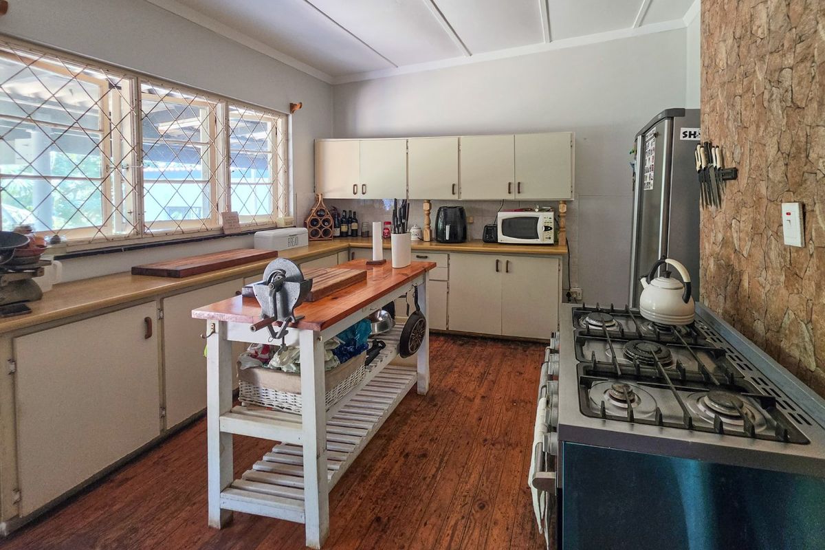A functional kitchen featuring timber flooring, stone feature wall, gas cooktop, and ample built-in cabinetry with a central prep island.