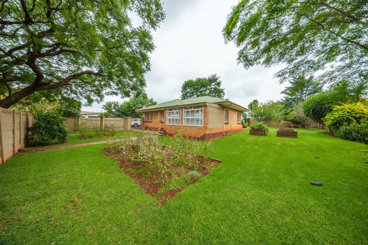 A view of the rear garden featuring a well-maintained lawn, established trees, and a brick-built house with a green metal roof.