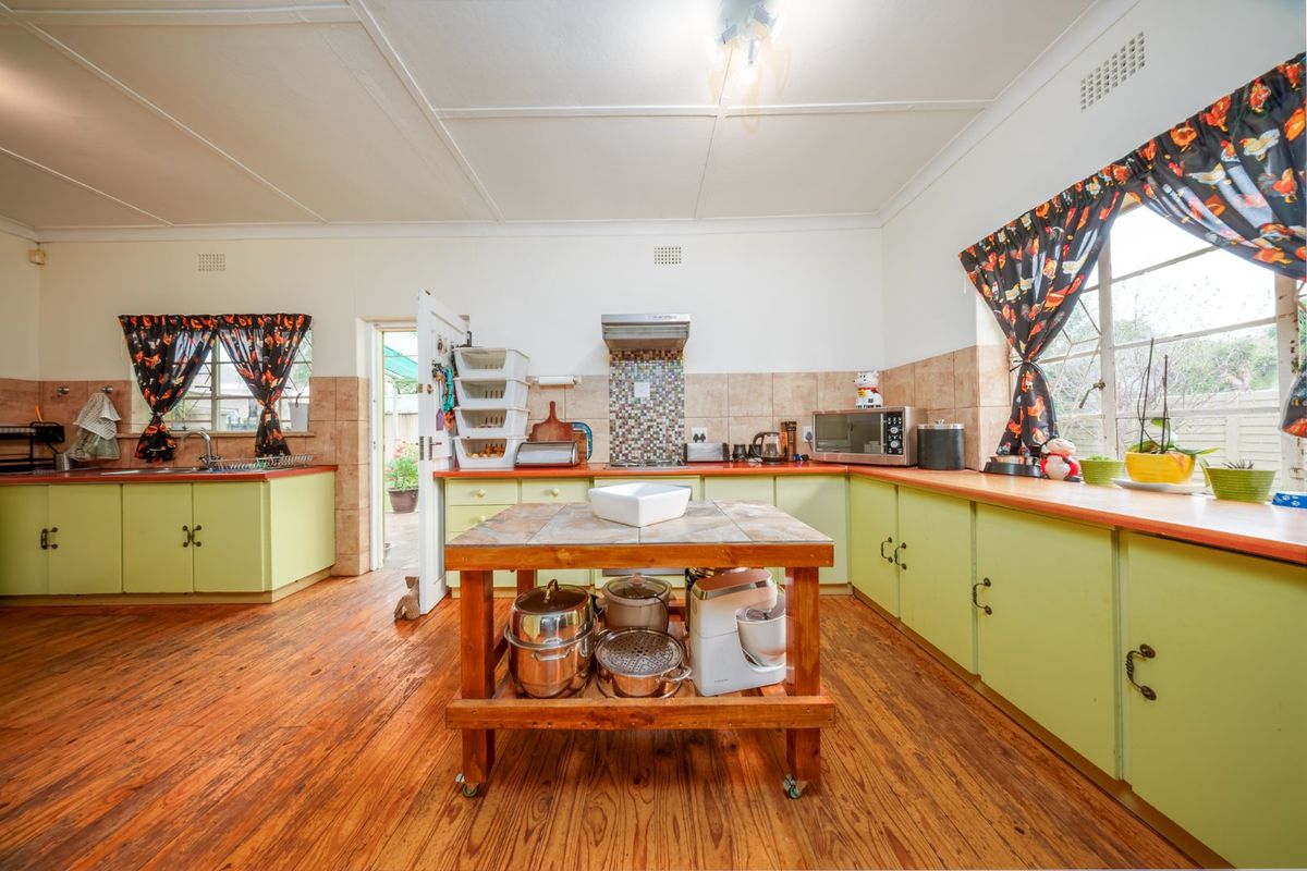 Spacious kitchen featuring wooden flooring, ample cabinetry, tiled splashbacks, and a central island, offering a functional layout with direct access to the exterior.