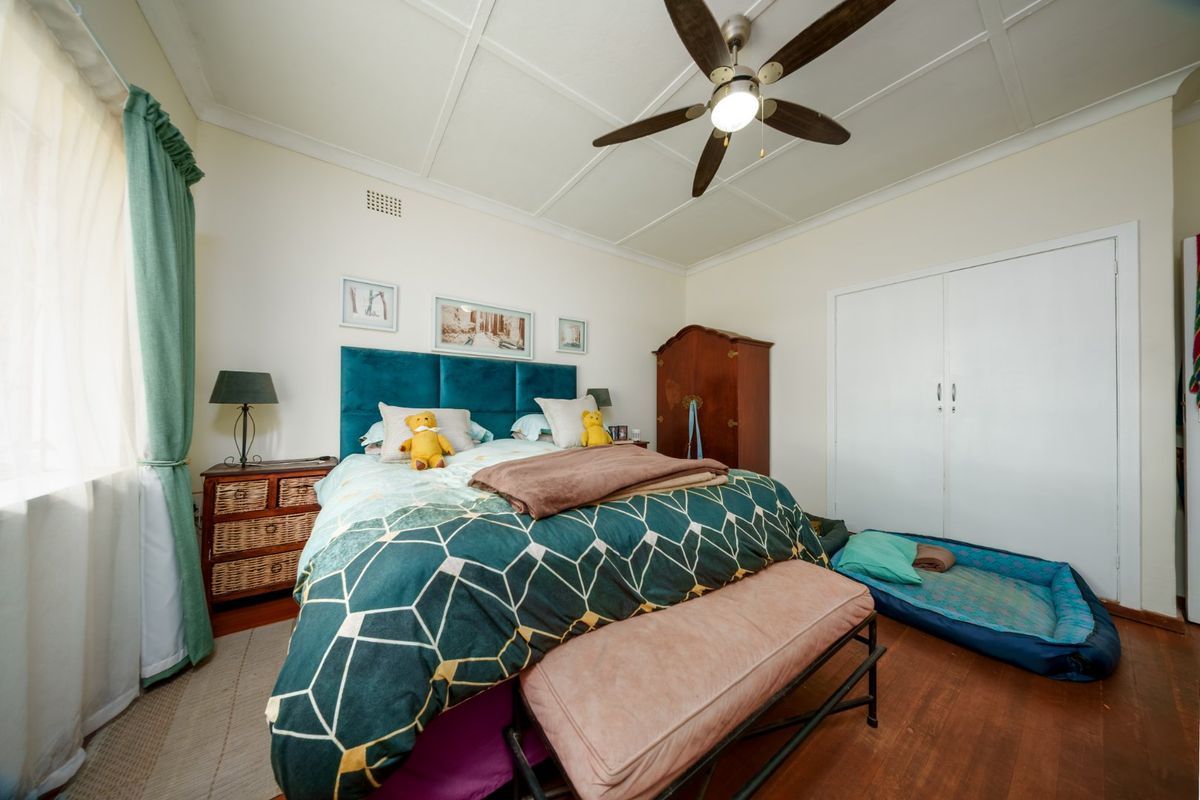A well-proportioned bedroom featuring original timber flooring, a ceiling fan, and built-in wardrobe storage.