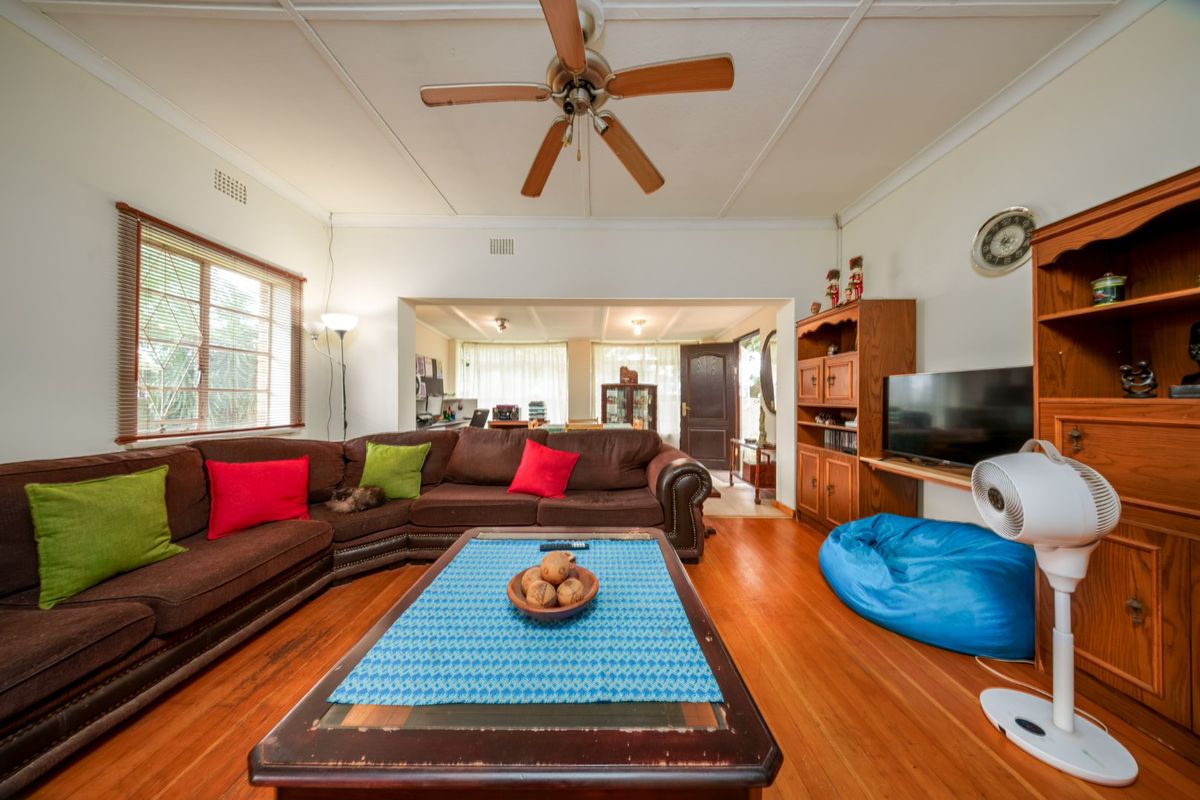 Spacious living room featuring polished timber flooring, a ceiling fan, and an open-plan layout connecting to the adjacent room.