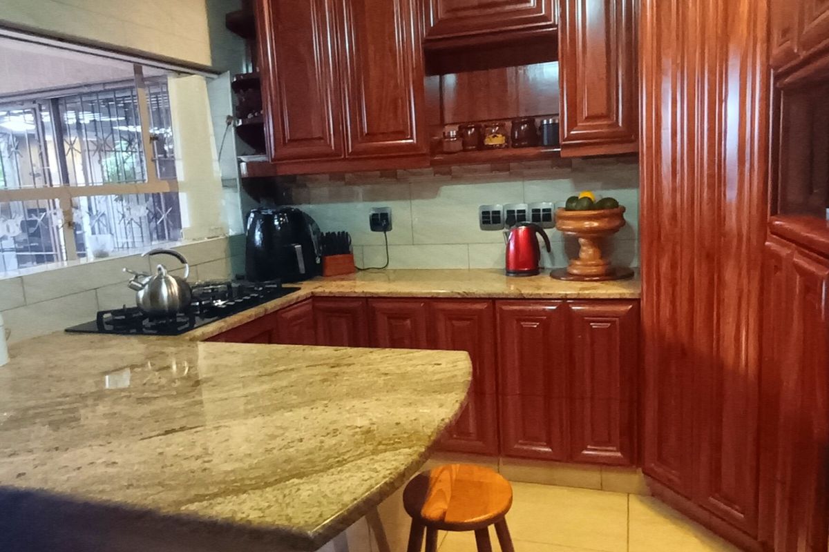 A functional kitchen featuring warm-toned wooden cabinetry, granite countertops, a gas hob, and tiled finishes, offering a classic and practical cooking space.