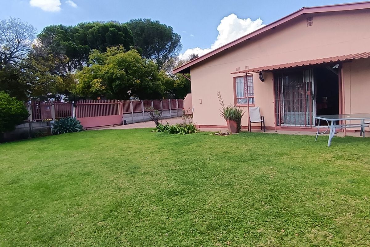 Rear view of the property featuring a spacious lawn, concrete patio area, and secure metal perimeter fencing.