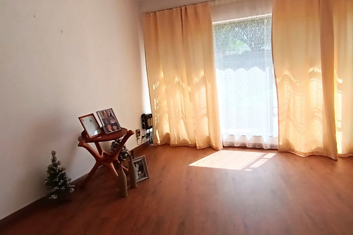 A bright, empty living room featuring laminate flooring and a large window with curtains, offering a blank canvas for personalization.