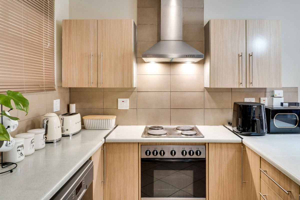 A functional kitchen featuring light wood-grain cabinetry, a tiled backsplash, and integrated stainless steel appliances including an electric hob and oven.