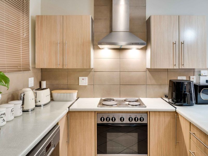 A functional kitchen featuring light wood-grain cabinetry, a tiled backsplash, and integrated stainless steel appliances including an electric hob and oven.