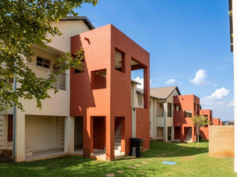 Exterior view of a modern apartment complex featuring red-toned architectural facades, private patios, balconies, and well-maintained communal garden spaces.
