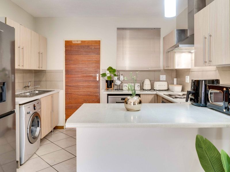 A functional kitchen featuring light wood-veneer cabinetry, tiled backsplash, integrated laundry plumbing, and a breakfast counter, providing a clean and practical workspace.