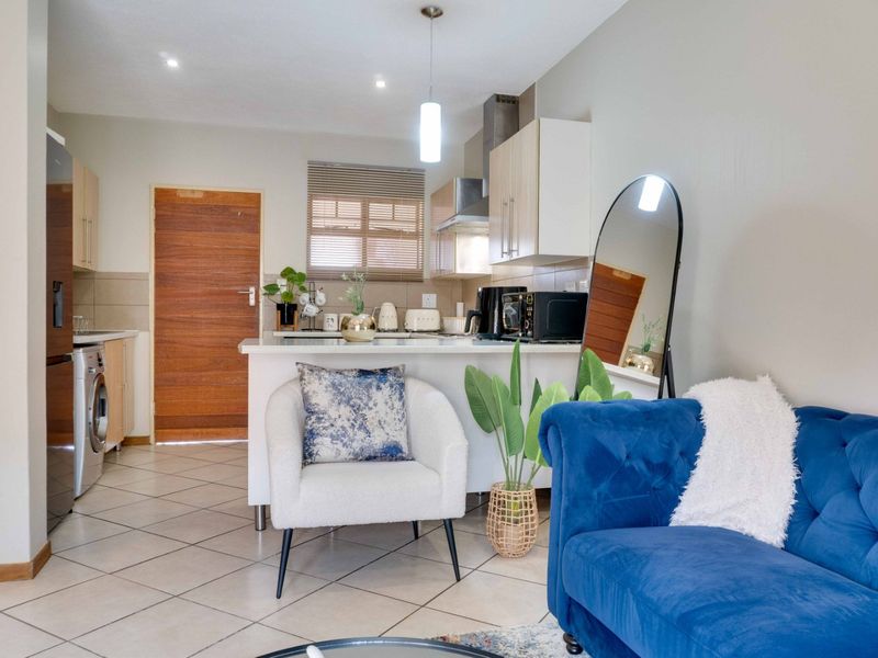 An open-plan living area featuring a functional kitchen with built-in cabinetry, tiled flooring, and modern lighting, seamlessly connected to the living space.