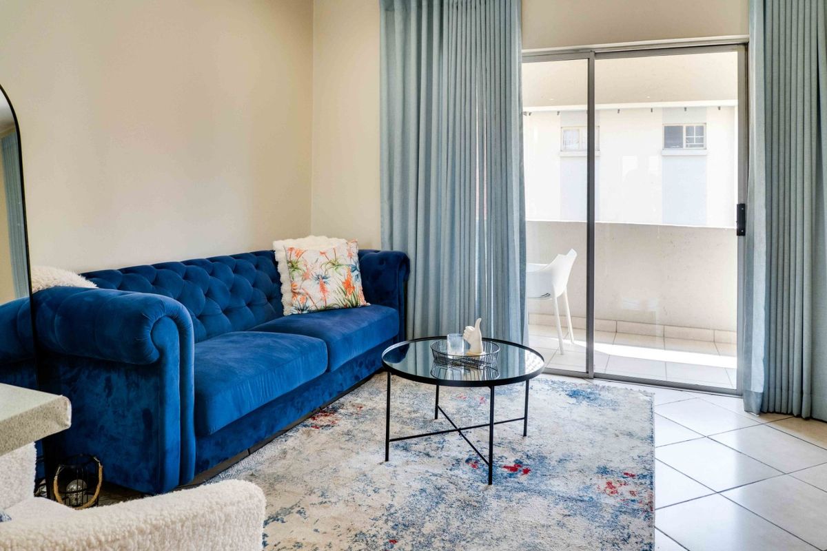 A bright living room featuring tiled flooring and a large sliding glass door providing access to an outdoor balcony area.