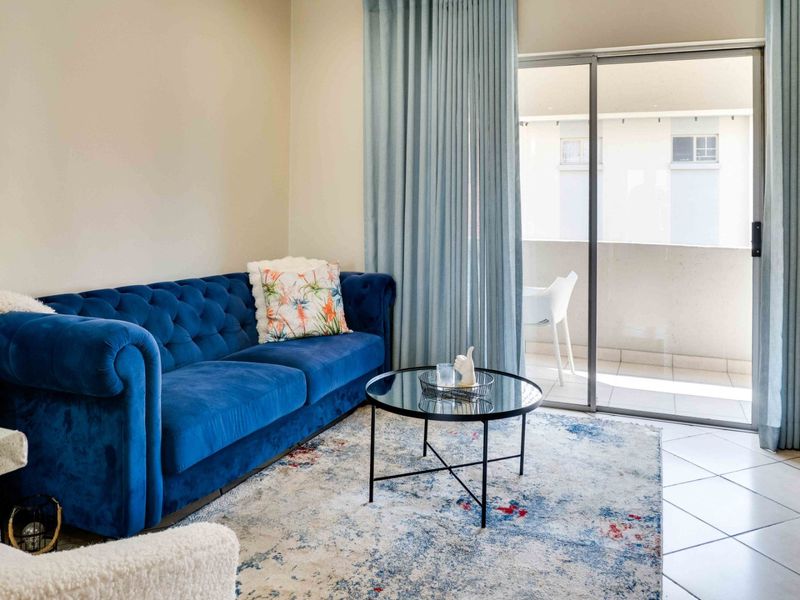 A bright living room featuring tiled flooring and a large sliding glass door providing access to an outdoor balcony area.