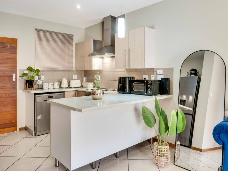 A modern kitchen featuring light wood cabinetry, a breakfast bar, tiled backsplash, and stainless steel extractor fan, offering a clean and functional cooking space.