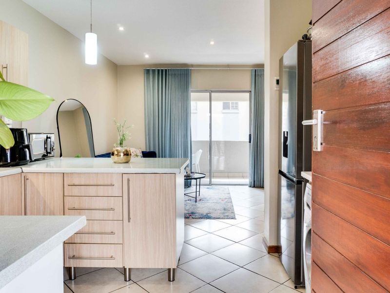 Open plan kitchen and living area featuring modern laminate cabinetry, stone countertops, tiled flooring, and direct access to a private balcony.