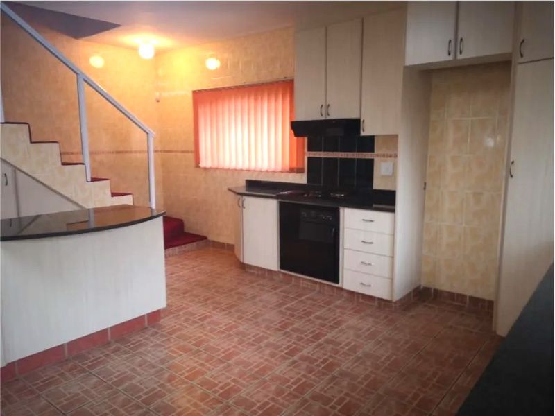 A dated kitchen featuring built-in cabinetry, an integrated oven, and a breakfast counter, adjacent to an internal staircase with tiled flooring throughout.