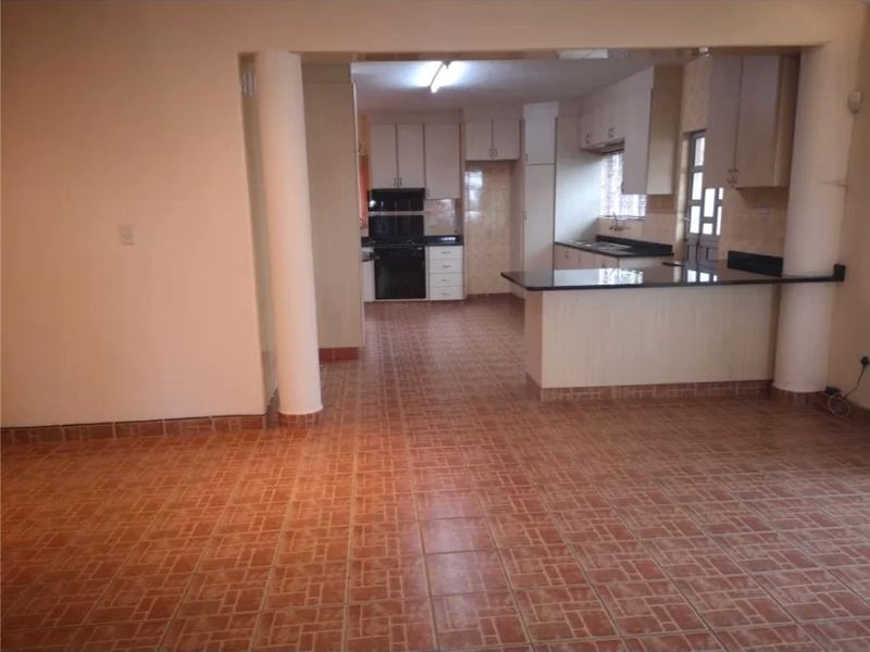Open plan kitchen and living area featuring tiled flooring, built-in cabinetry with granite countertops, and structural support columns.