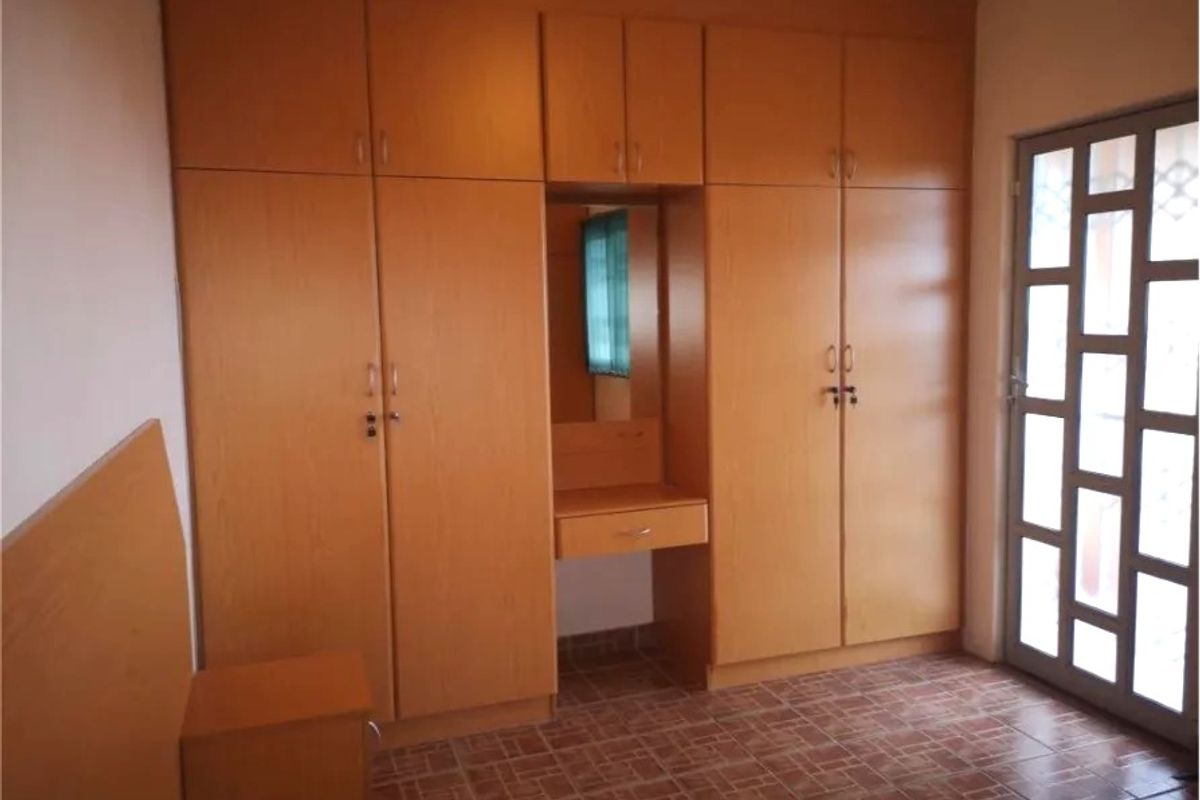 A bedroom featuring extensive built-in wooden cupboards with an integrated vanity unit, tiled flooring, and a glass-paneled door leading outside.