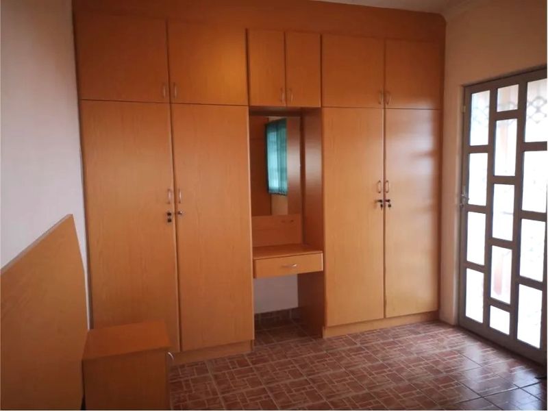 A bedroom featuring extensive built-in wooden cupboards with an integrated vanity unit, tiled flooring, and a glass-paneled door leading outside.