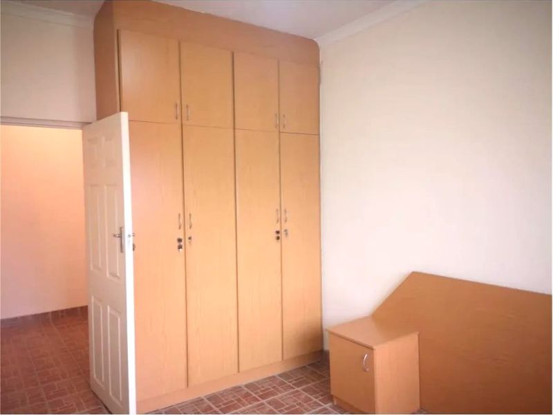 A bedroom featuring built-in wooden cupboards and tiled flooring, offering a clean and functional space ready for personalization.