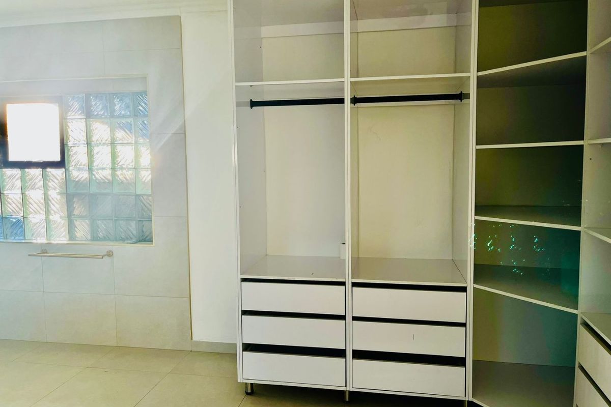 A bright bedroom featuring modern white built-in cupboards, tiled flooring, and a decorative glass block window.