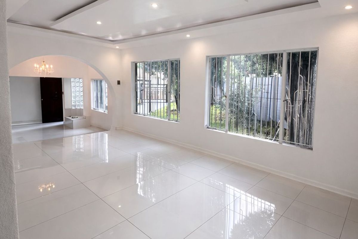 Spacious, bright living area featuring polished porcelain floor tiles, a modern recessed ceiling with downlights, and an elegant archway leading to an adjacent space.