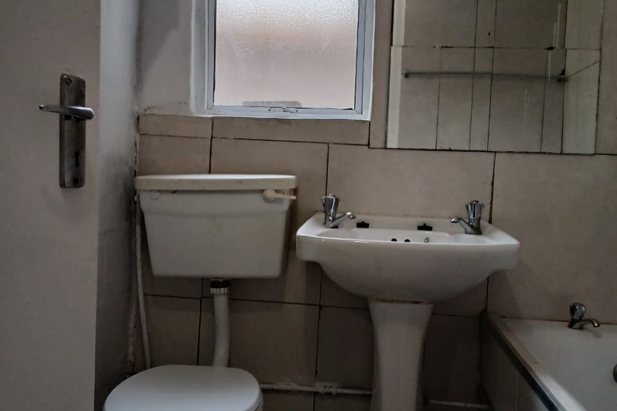 A compact bathroom featuring a pedestal basin, toilet, and bathtub with dated wall tiling and a frosted glass window.