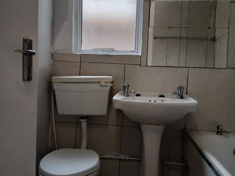 A compact bathroom featuring a pedestal basin, toilet, and bathtub with dated wall tiling and a frosted glass window.
