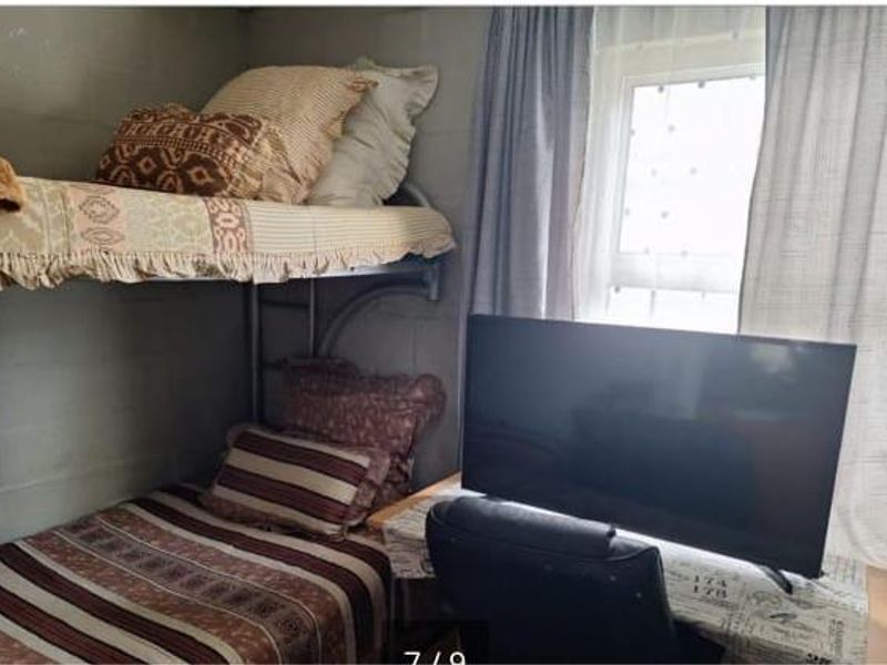 A compact bedroom featuring exposed concrete block walls and a window with curtains.