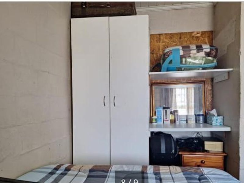 A compact bedroom featuring a built-in white wardrobe and integrated shelving unit with exposed blockwork walls.