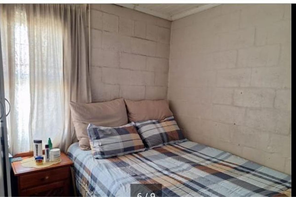 A compact bedroom featuring exposed concrete block walls and a single window with curtains.